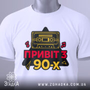 Футболка привіт з 90-х, біла, складена на поверхні, фон світло-сірий, принт з касетою та написом 'ПРИВІТ З 90-х' у червоному та жовтому кольорах, з етикеткою на комірці.