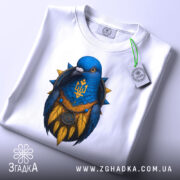 Футболка птах тризуб білого кольору, зображена зверху, на ній видно етикетку, фон світлий, принт з птахом синього кольору з жовтими деталями та гербом України.