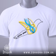 Футболка птах волі білого кольору, складена на столі, ракурс зверху, фон світло-сірий, принт з птахом у жовтих та блакитних тонах, напис 'птах волі' на стрічці, з етикеткою зеленого кольору.