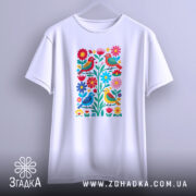 Футболка пташки у квітах, біла, підвішена на вішалці, фон світло-сірий, принт з яскравими пташками і квітами, деталі чітко видимі.