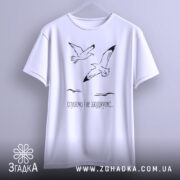 Футболка пташина свобода, білого кольору, підвішена на вішалці, фон світло-сірий, принт з двома птахами, що летять, та текстом "слухаємо і не засуджуємо..." під ними.