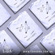 Футболка пташина свобода, білого кольору, зображена з правого ракурсу на манекені, фон світло-сірий, принт з двома птахами, що летять, та текстом "слухаємо і не засуджуємо..." під ними.