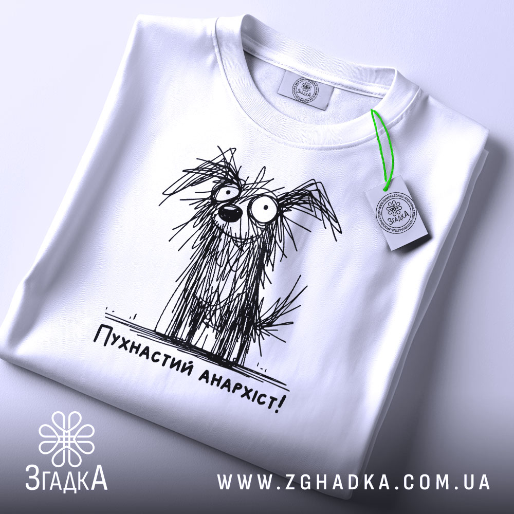 Футболка пухнастий анархіст, білого кольору, складена на плоскій поверхні, фон світло-сірий, принт з малюнком пухнастого собаки з великими очима та написом 'Пухнастий анархіст!' під ним, з етикеткою на зеленому шнурку.