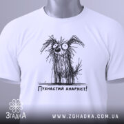 Футболка пухнастий анархіст, білого кольору, складена на плоскій поверхні, фон світло-сірий, принт з малюнком пухнастого собаки з великими очима та написом 'Пухнастий анархіст!' під ним, з етикеткою на зеленому шнурку.