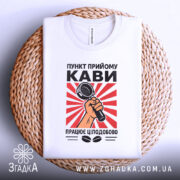 Футболка пункт прийому кави, біла, складена на плетеному кошику, фон світлий, принт з червоними променями та мікрофоном у руці.