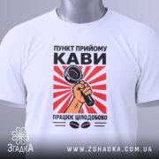 Футболка пункт прийому кави, біла, складена на столі, фон світлий, принт з червоними променями та мікрофоном у руці, на комірці зелена етикетка.