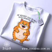 Футболка пузіко нажріть своє, біла футболка, зображена зверху, фон світло-сірий, принт з котом, що усміхається, текст українською мовою, на футболці є етикетка.