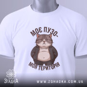 Футболка пузо терапія, складена біла футболка, зображена з верхнього ракурсу, фон світлий, принт з котом у куртці, текст "МОЄ ПУЗО- МОЯ ТЕРИТОРІЯ" в коричневому кольорі, на футболці є етикетка з зеленим шнурком.