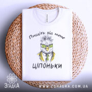 Футболка пищіть від мене. Біла футболка, складена на плетеній кошику. Принт з малюнком птаха в окулярах та жовтому піджаку, текст "Ціпоньки". Фон натуральний, з текстури кошика.