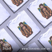 Футболка письменник Шевченко, біла, зображена на манекені, фон світло-сірий, принт з зображенням чоловіка в традиційному одязі з вусами та шапкою, на фоні жовто-блакитний прапор.