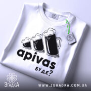 Футболка пивний гумор, біла, зображена зверху на плоскій поверхні, фон світло-сірий, принт з трьома пивними кухлями з пінкою та текстом 'apivas буде?', з зеленим ярликом.
