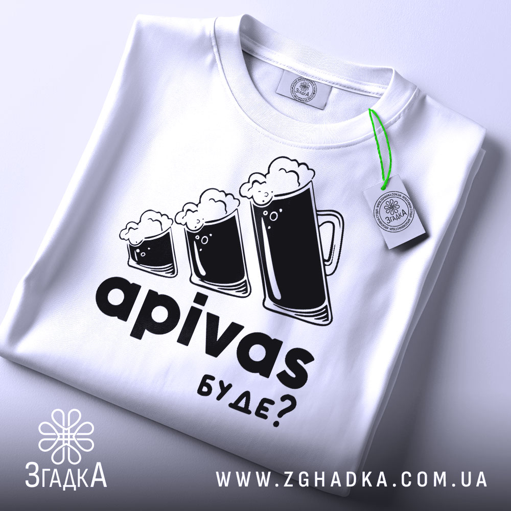 Футболка пивний гумор, біла, зображена зверху на плоскій поверхні, фон світло-сірий, принт з трьома пивними кухлями з пінкою та текстом 'apivas буде?', з зеленим ярликом.