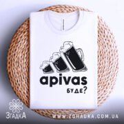 Футболка пивний гумор, біла, зображена зверху на плоскій поверхні з плетеним елементом, фон світло-сірий, принт з трьома пивними кухлями з пінкою та текстом 'apivas буде?' у чорному кольорі.