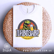 Футболка пивозавр пінний період, біла, зображена зверху на плетеній основі, фон світлий, принт з динозавром, що тримає пиво, кольори яскраві, текст чорний з жовтими акцентами.