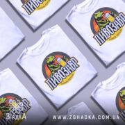 Футболка пивозавр пінний період, біла, зображена з фронтального ракурсу на манекені, фон нейтральний, принт з динозавром, що тримає пиво, кольори яскраві, текст чорний з жовтими акцентами.