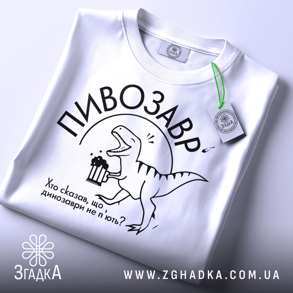 Футболка пивозавр білого кольору, складена на поверхні, фон світлий, принт з динозавром, що тримає пиво, текст: "Хто сказав, що динозаври не п'ють?", на футболці є етикетка з зеленим шнурком.