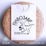 Футболка пивозавр білого кольору, складена на плетеній основі, фон світлий, принт з веселим динозавром, що тримає пиво, текст: "Хто сказав, що динозаври не п'ють?"