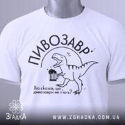 Футболка пивозавр білого кольору, складена на поверхні, фон світлий, принт з динозавром, що тримає пиво, текст: "Хто сказав, що динозаври не п'ють?", на футболці є етикетка з зеленим шнурком.