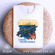 Футболка ракета фламінго, біла, складена на плетеній кошику, з верхнього ракурсу, фон білий, принт зображує ракету та текст "3,000km CRUISE MISSILE" у жовтому та блакитному кольорах.
