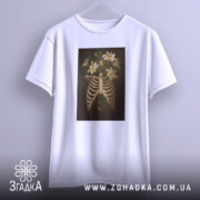 Футболка ребра розквітли, біла футболка з принтом, що зображує скелетні ребра з ліліями, підвішена на вішалці, з нейтральним фоном, з фронтального ракурсу.