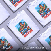 Футболка Рембо перша кров білого кольору, зображена з фронтального ракурсу на манекені, фон світло-сірий, принт містить яскраві кольори з персонажами та написом 'FIRST BLOOD'.