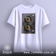 Футболка ретро касета білого кольору, зображена на вішалці, ракурс спереду, фон світло-сірий, принт з касетою з жовтими котушками, деталі принта чітко видимі.