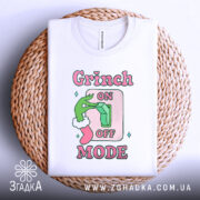 Футболка режим Грінча, біла, зображена зверху на плетеній кошику, фон світлий, принт з зеленим рукою Грінча, що натискає на вимикач, текст 'ON OFF MODE' в рожевих і зелених кольорах.