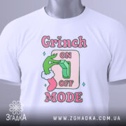 Футболка режим Грінча, біла, зображена зверху, фон світлий, принт з зеленим рукою Грінча, що натискає на вимикач, текст 'ON OFF MODE' в рожевих і зелених кольорах, з біркою на шнурку.