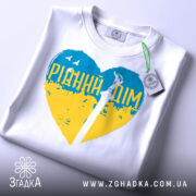 Футболка рідний дім, біла, складена на столі, фон світло-сірий, принт у формі серця з жовто-блакитними кольорами та написом 'РІДНИЙ ДІМ', з етикеткою на комірці.