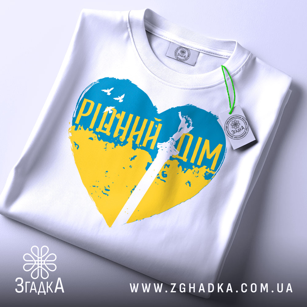 Футболка рідний дім, біла, складена на столі, фон світло-сірий, принт у формі серця з жовто-блакитними кольорами та написом 'РІДНИЙ ДІМ', з етикеткою на комірці.