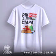 Футболка рік новий, біла, підвішена на вішалці, фон градієнтний сірий, принт з оленем у червоному капелюсі, ялинкою та подарунками, текст "РІК новий А ЛІНЬ СТАРА".