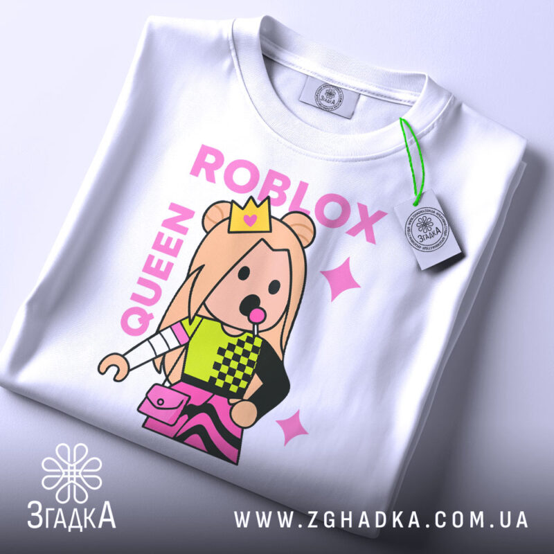 Футболка Roblox королева, біла, зображена на столі, фон світлий, принт з персонажем у короні, кольорові деталі на одязі, текст 'ROBLOX QUEEN' у рожевому кольорі, з етикеткою.