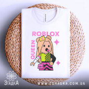 Футболка Roblox королева, біла, зображена на плетеному кошику, фон світлий, принт з персонажем у короні, кольорові деталі на одязі, текст 'ROBLOX QUEEN' у рожевому кольорі.