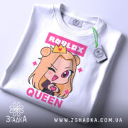 Футболка Roblox королева білого кольору, складена на поверхні, фон світло-сірий, принт з аніме персонажем з короною та написом 'ROBLOX QUEEN' у рожевих тонах, з етикеткою на комірці.