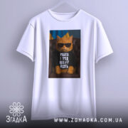 Футболка робота і труд. Біла футболка підвішена на вішалці, з принтом кота в окулярах на фоні українського прапора. Видно деталі принта та текст.