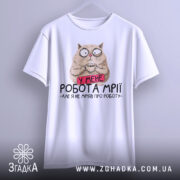 Футболка робота мрії, білого кольору, підвішена на вішалці, фон світло-сірий, принт з котом, який тримає чашку, з текстом 'У МЕНЕ РОБОТА МРІЇ - АЛЕ Я НЕ МРІЯВ ПРО РОБОТУ'.