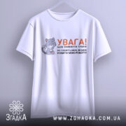 Футболка робити мою роботу. Біла футболка з коротким рукавом, підвішена на вішалці. На фоні світло-сірий колір. Принт містить малюнок котика з ножицями та текстом, що попереджає про обережність.