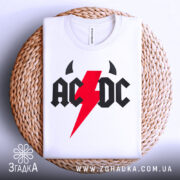 Футболка рок енергія, біла, складена на плетеній основі, фон світло-сірий, принт з червоним блискавкою та чорними літерами 'AC/DC'.
