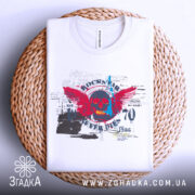 Футболка рок естетика, біла, складена на плетеній кошику, фон світло-сірий, принт з черепом, червоними крилами та текстом, видима етикетка.