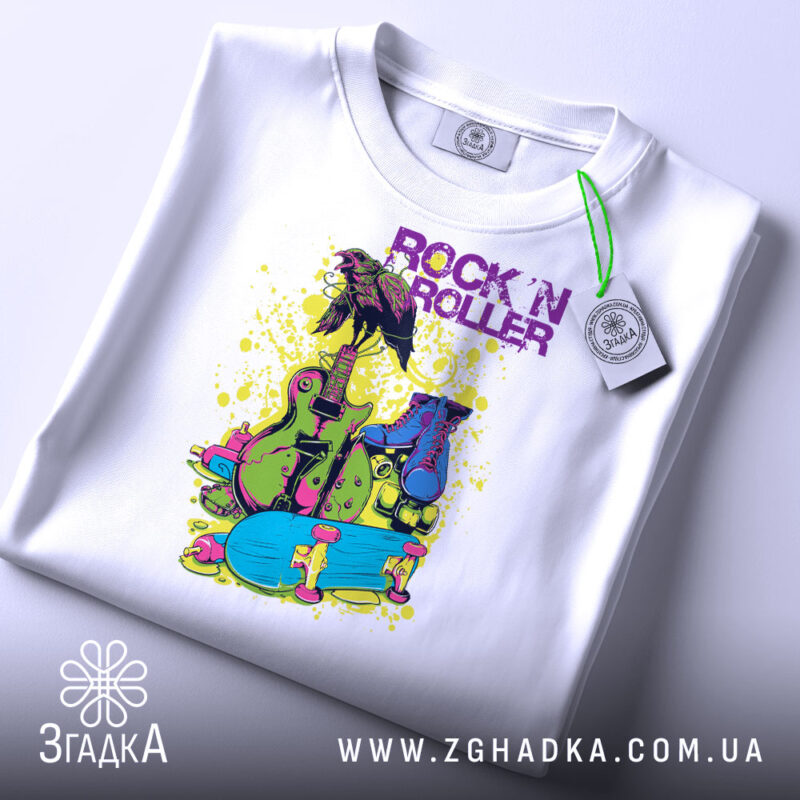 Футболка рок і арт білого кольору, складена на поверхні, зображена зверху, фон світло-сірий, принт яскравий з елементами: гітара, роликові ковзани та напис 'ROCK 'N ROLLER' у фіолетовому кольорі, на футболці є етикетка.
