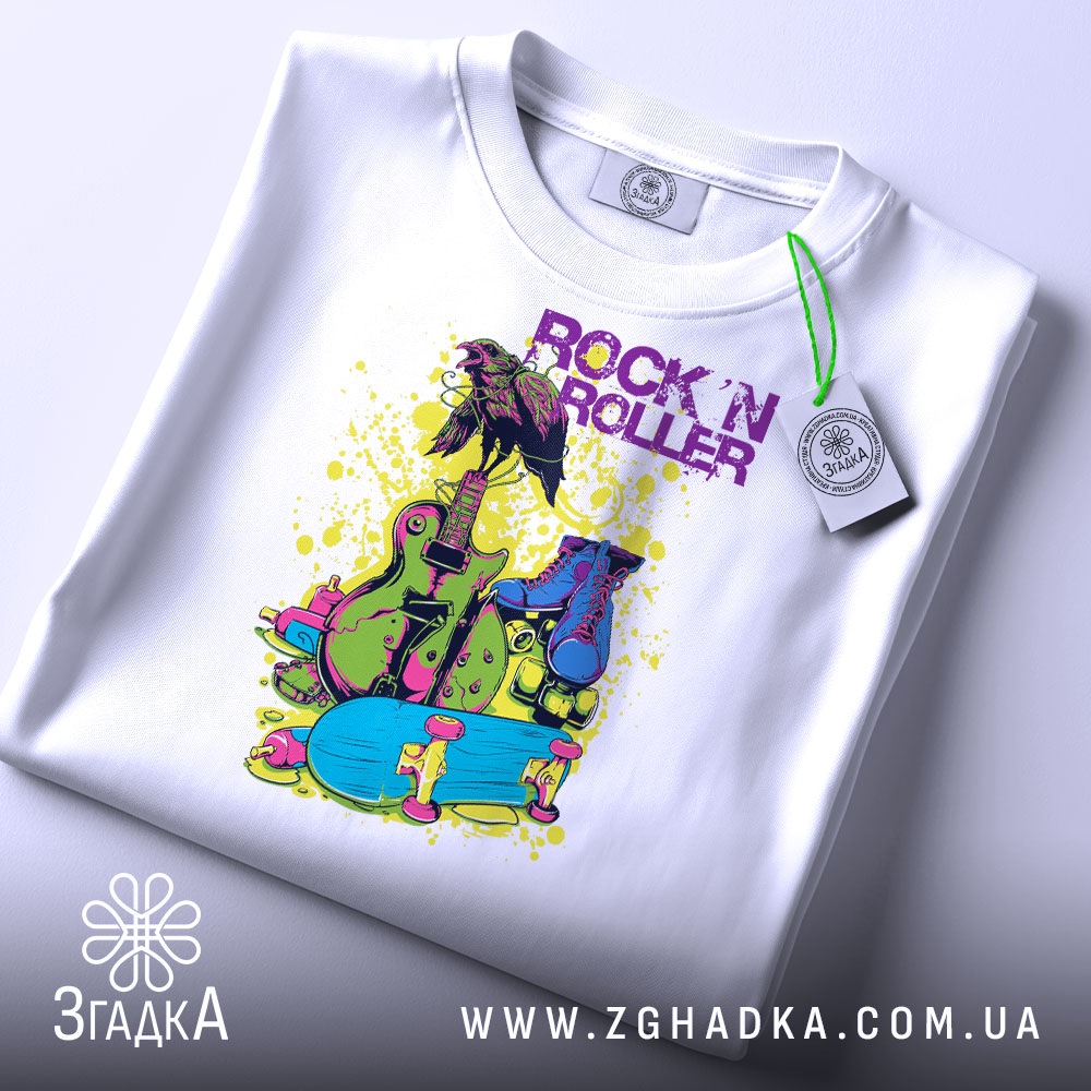 Футболка рок і арт білого кольору, складена на поверхні, зображена зверху, фон світло-сірий, принт яскравий з елементами: гітара, роликові ковзани та напис 'ROCK 'N ROLLER' у фіолетовому кольорі, на футболці є етикетка.