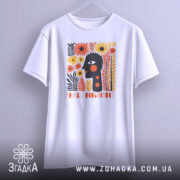 Футболка розквіт особистості. Біла футболка з коротким рукавом, підвішена на вішалці. На фоні світло-сірий колір. Принт з абстрактним обличчям, оточеним яскравими квітами, виконаний в червоних, жовтих і чорних тонах.