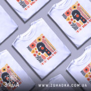 Футболка розквіт особистості. Біла футболка з коротким рукавом, зображена на манекені. На фоні світло-сірий колір. Принт містить абстрактне обличчя з чорними рисами, червоними крапками та яскравими квітами в оранжевих і жовтих тонах.