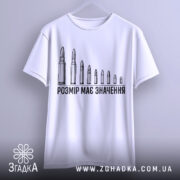 Футболка розмір має значення, біла, підвішена на вішалці, фон світлий, принт з дев'яти патронів, текст чорного кольору, рукави широкі.