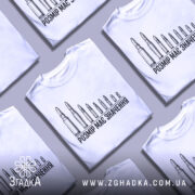 Футболка розмір має значення, біла, зображена на манекені, фон нейтральний, принт з дев'яти патронів різного розміру, текст чорного кольору під принтом.