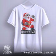 Футболка розшукується Санта. Біла футболка, висяча на вішалці, з принтом Санти, який радісно піднімає руку. Фон світло-сірий, з легким градієнтом.