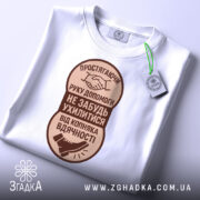 Футболка рука допомоги, білого кольору, розкладена на поверхні, фон світло-сірий, принт коричневого кольору з текстом та зображенням руки і ноги, на футболці є етикетка з зеленим шнурком.