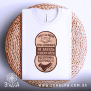 Футболка рука допомоги, білого кольору, розкладена на плетеній основі, фон натуральний, принт коричневого кольору з текстом та зображенням руки і ноги.