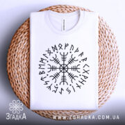 Футболка руни вікінгів, біла, складена на плетеній кошику, фон світлий, принт з чорними рунами у формі кола.