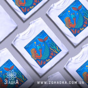 Футболка русалка читає, біла, з фронтальним ракурсом, на фоні світло-сірого, принт з русалкою, яка читає книгу, оточена водоростями та морськими елементами, яскраві кольори: блакитний, зелений, оранжевий.